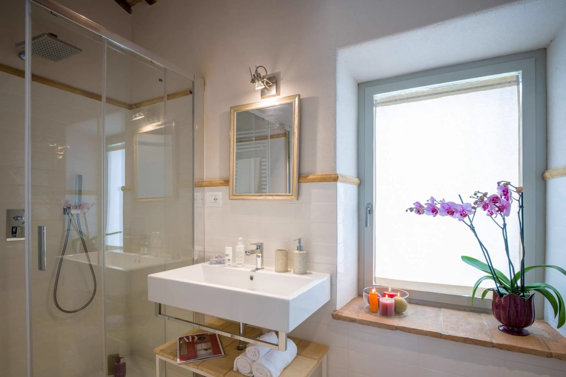 A bathroom with a tiled shower, a mirror and folded towels.