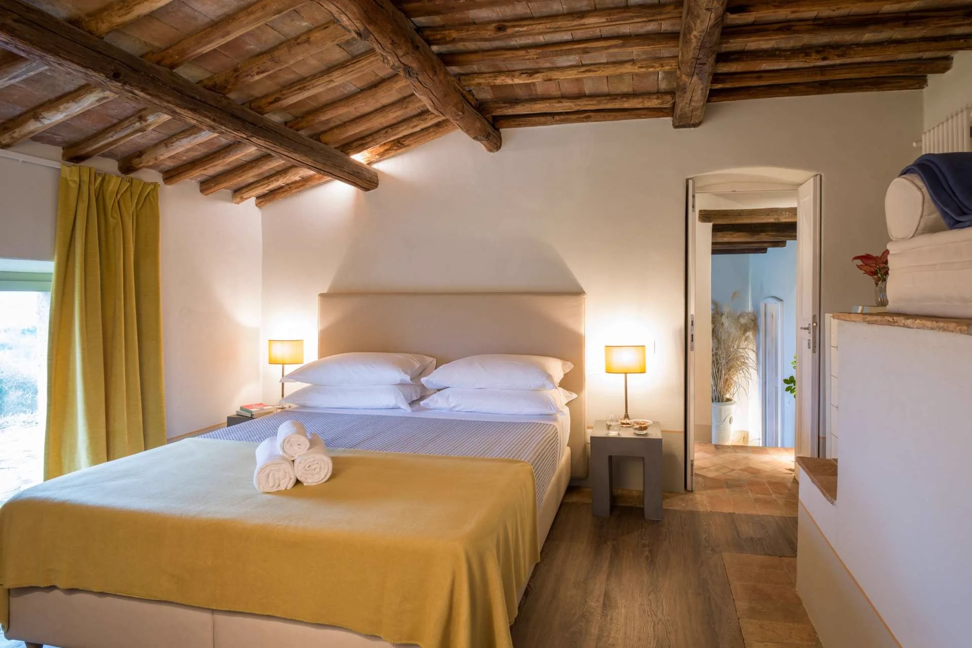 A bedroom with a wooden bed, warm textiles and a window onto the grounds.