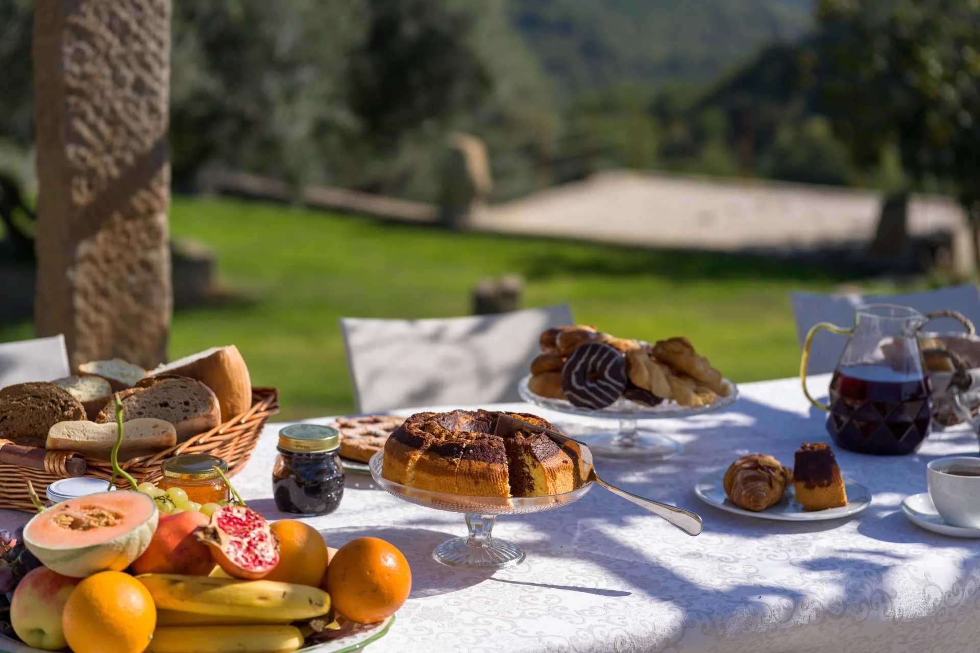 A breakfast table with coffee, bread, jam and fruit in morning light.