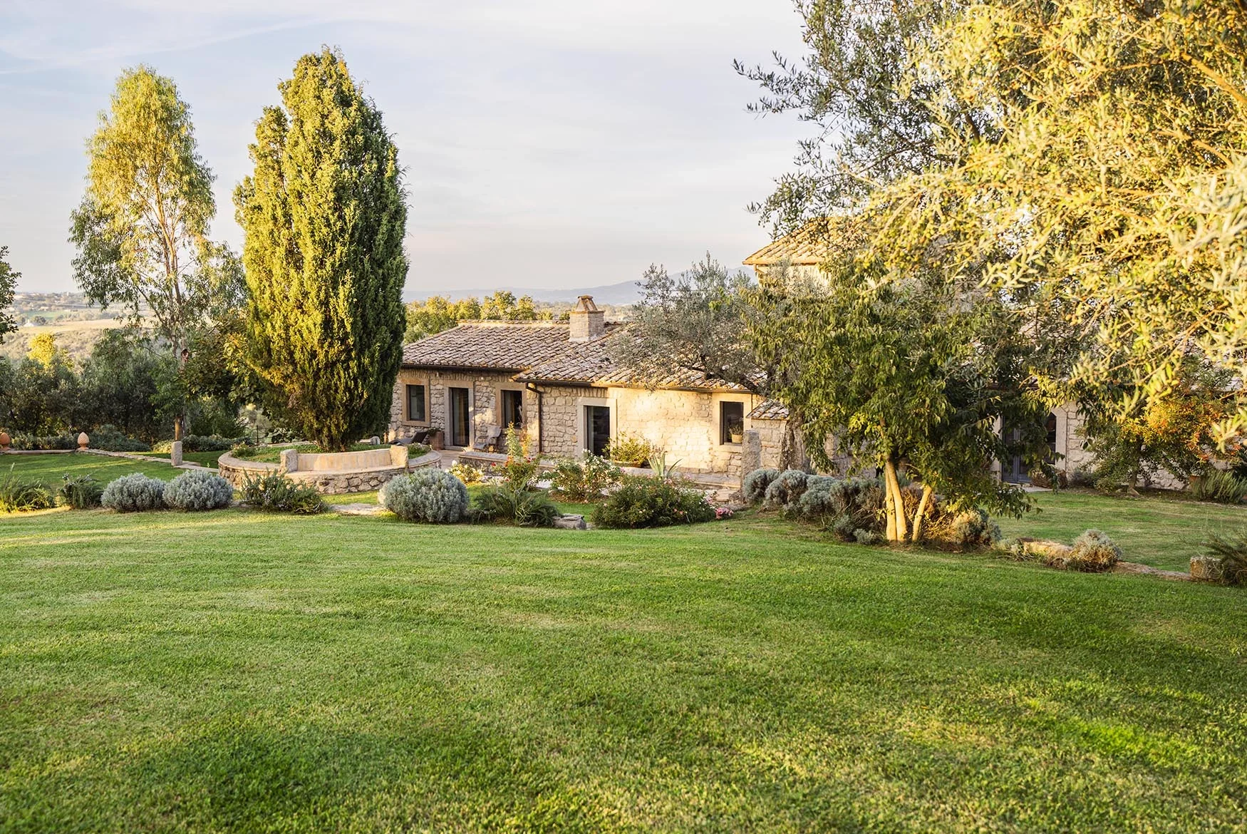 The Elaios residence in daylight: stone walls, shuttered windows and olive trees around it.