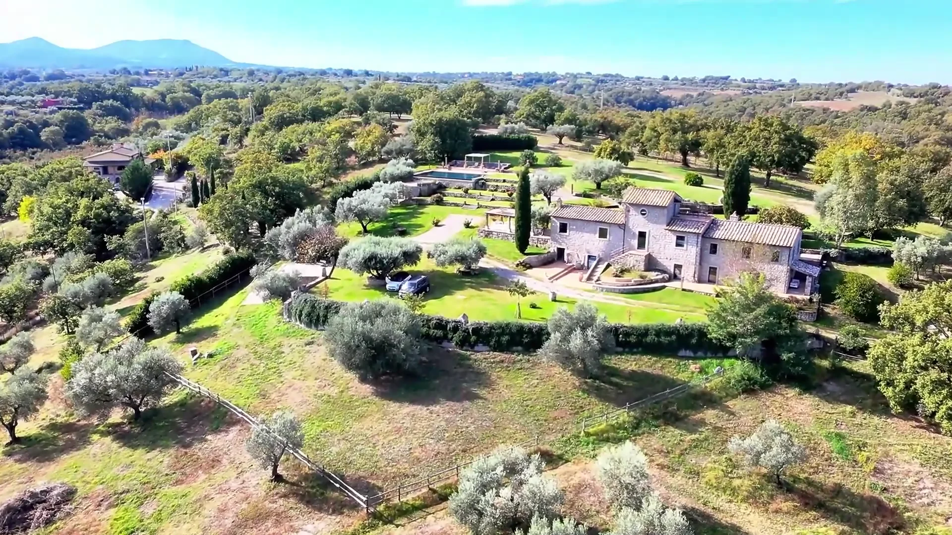 The gardens of Tenuta Villa Lavinia in low afternoon light: the pool, cypresses and the stone house beyond.