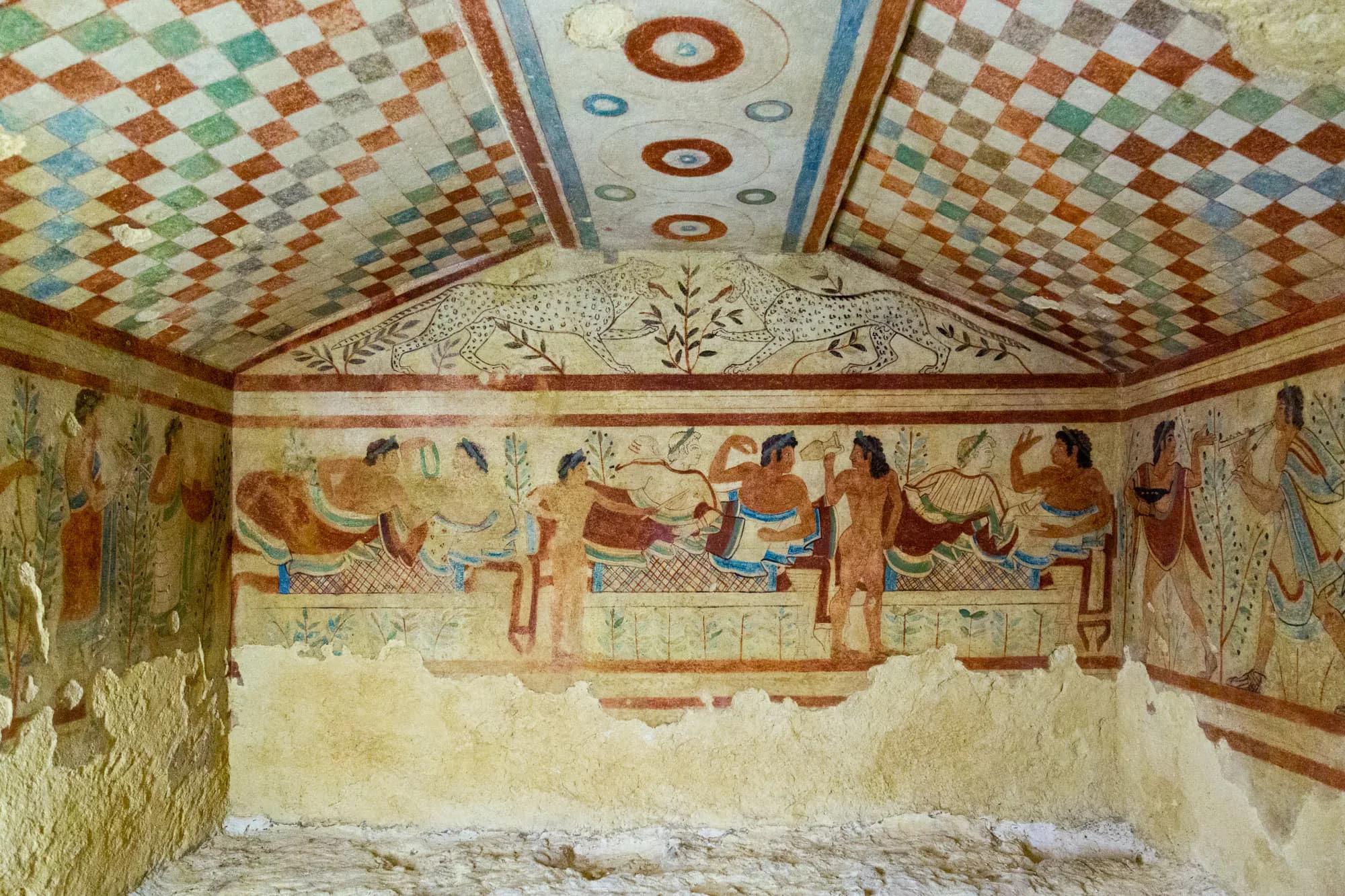 A painted Etruscan tomb chamber with figures on the plastered wall.