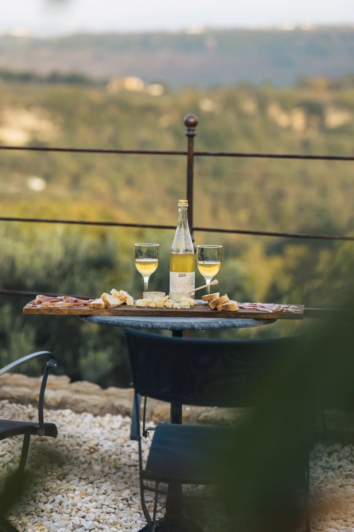 Two glasses of white wine and a platter of local food on a table outdoors.
